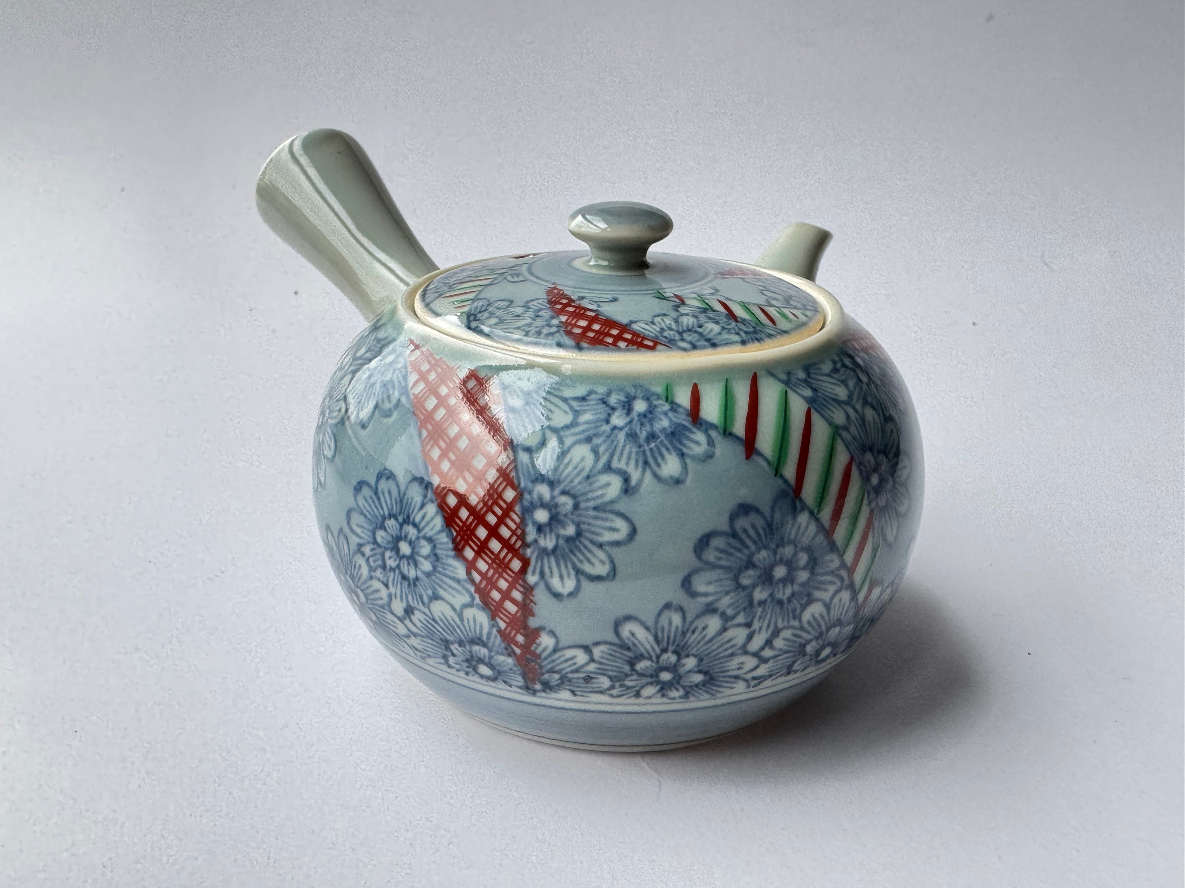Ceramic teapot with floral and striped patterns on a white background