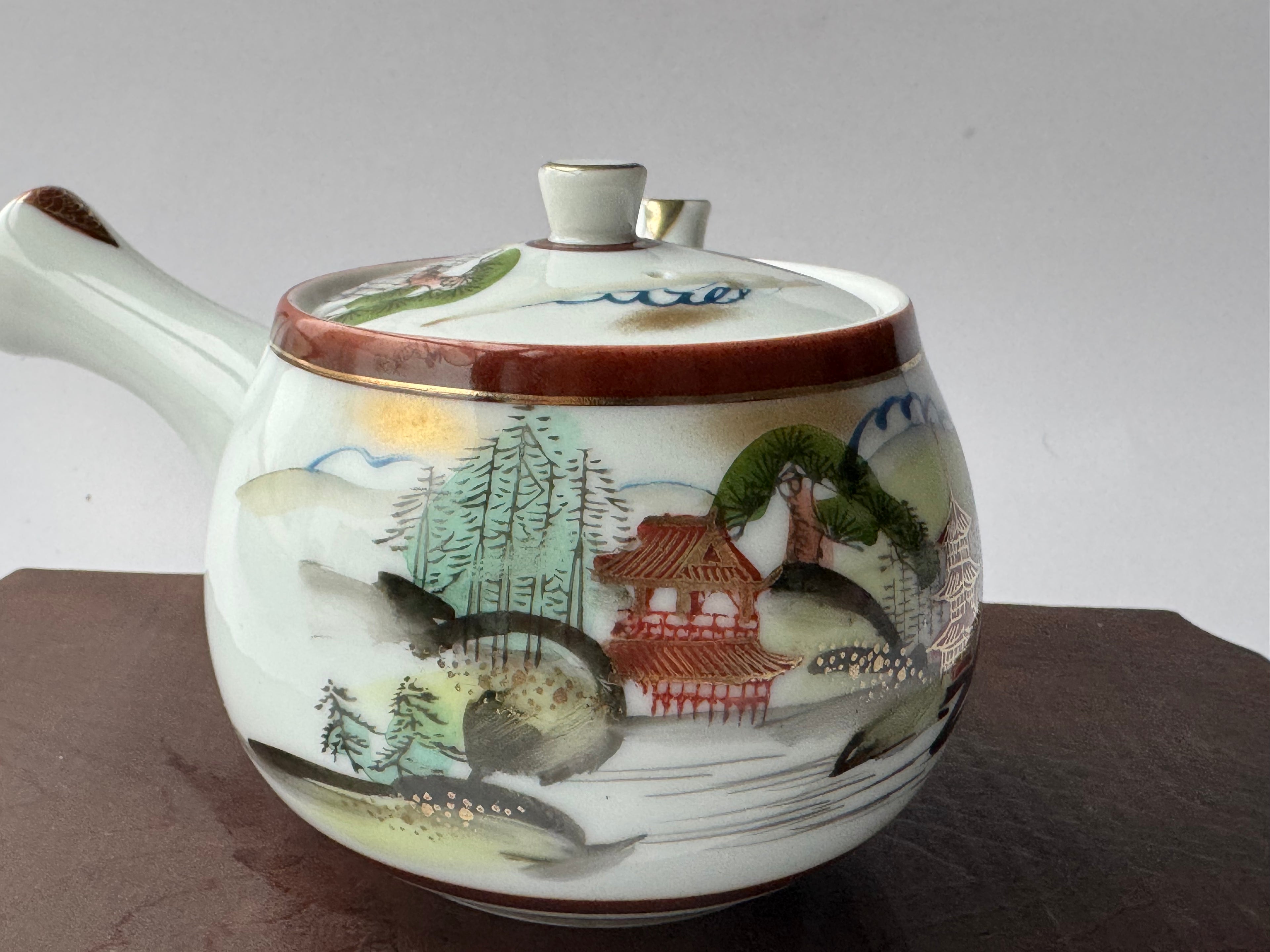 Decorative teapot with scenic design on a plain background