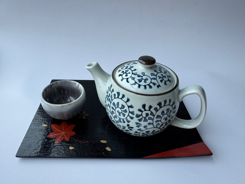 Ceramic teapot and cup with blue floral patterns on a black tray with red accents.