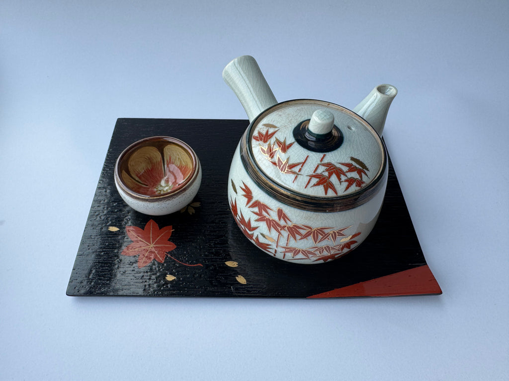 Ceramic teapot and bowl with floral design on a black tray against a white background