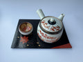 Ceramic teapot and bowl with floral design on a black tray against a white background