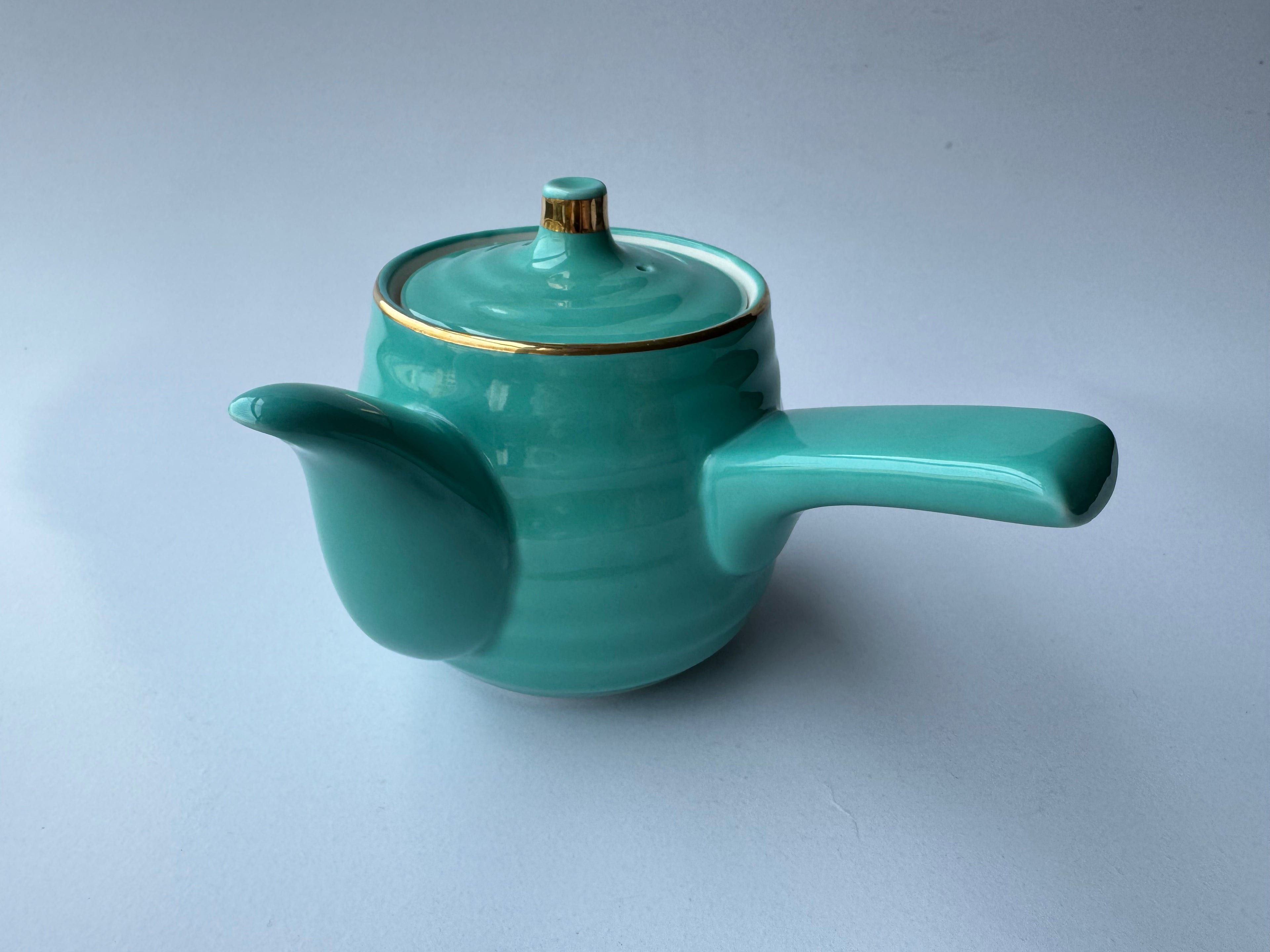 Turquoise teapot with gold rim on a light gray background