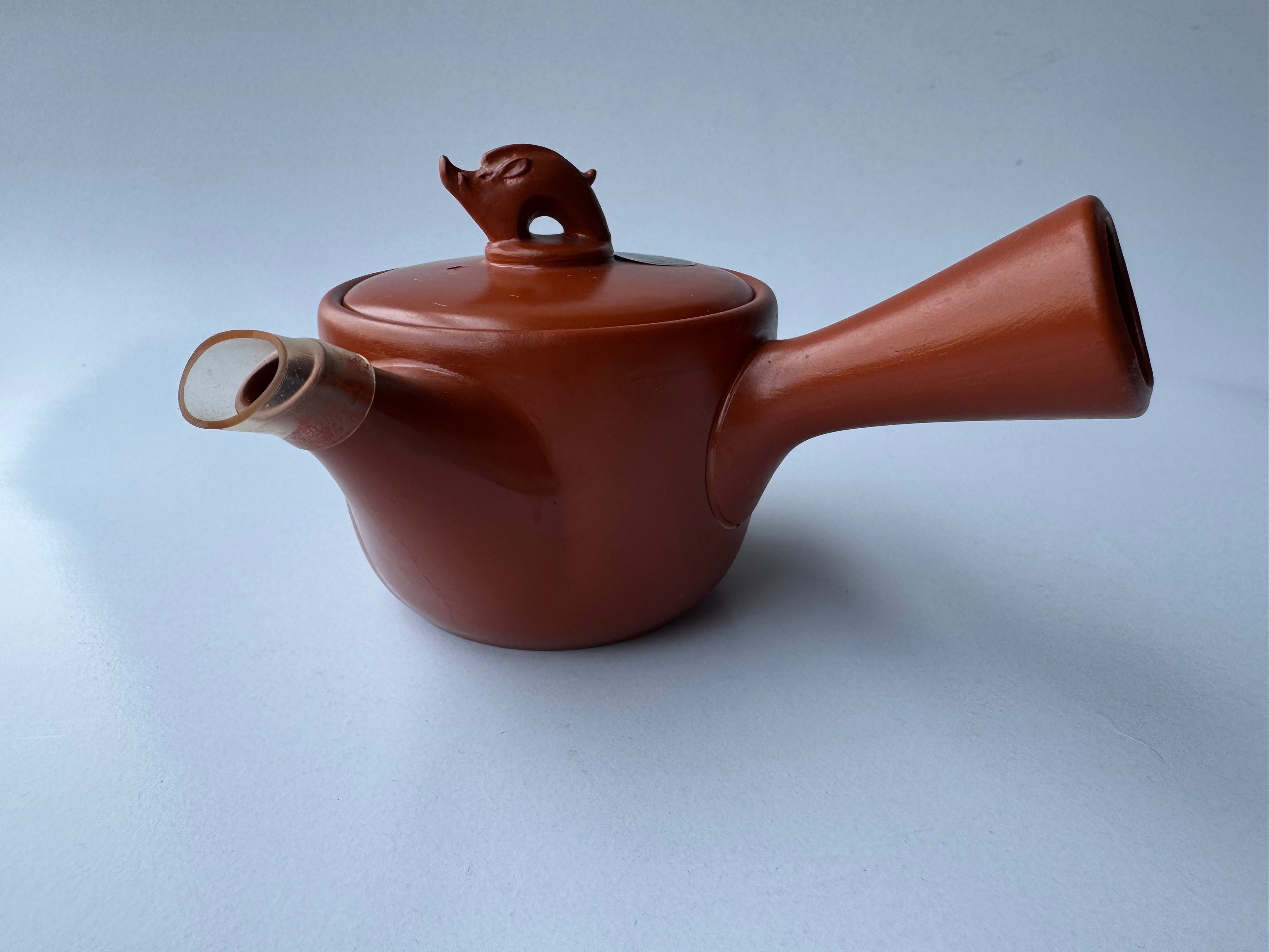 Red ceramic teapot with a lid on a light blue background