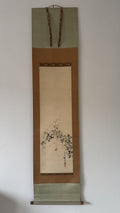 Traditional Japanese hanging scroll with floral design on a plain wall.