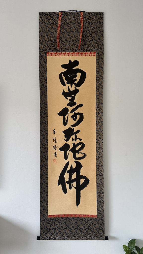 Traditional calligraphy scroll on a decorative frame against a white wall