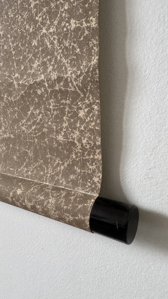 Roll of textured brown wallpaper with a black roller on a light gray background