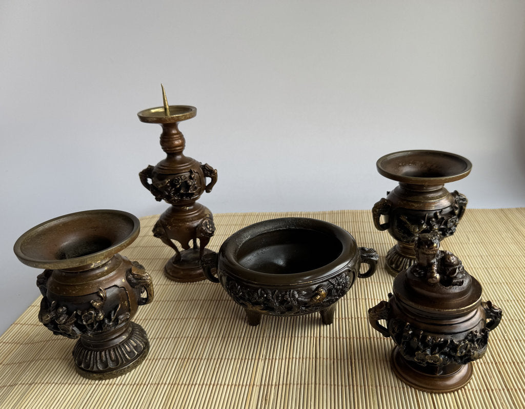 Set of five ornate bronze candle holders on a woven mat.
