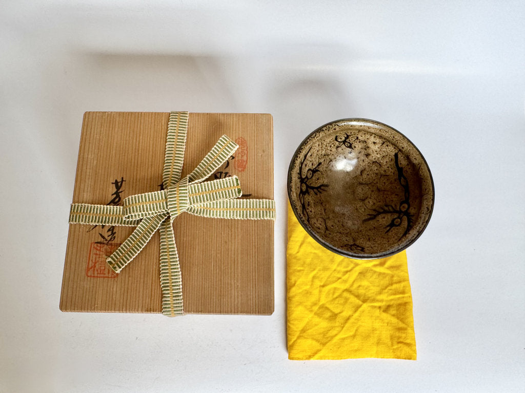 Gift wrapped in brown paper with a bow next to a ceramic bowl on a white background