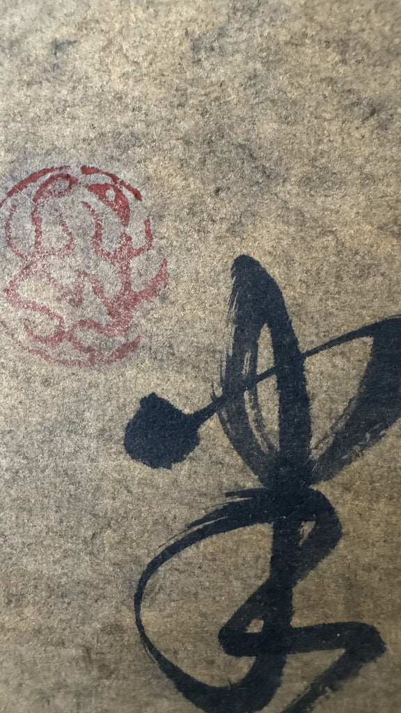 Close-up of textured beige paper with a large black calligraphic stroke and a faint red seal mark.