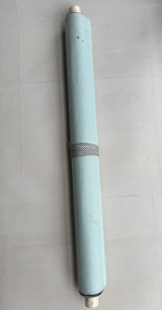 A light blue cylindrical product, possibly a pen, roller, or tube, with a textured metallic band around the middle, resting on a light gray tiled surface.