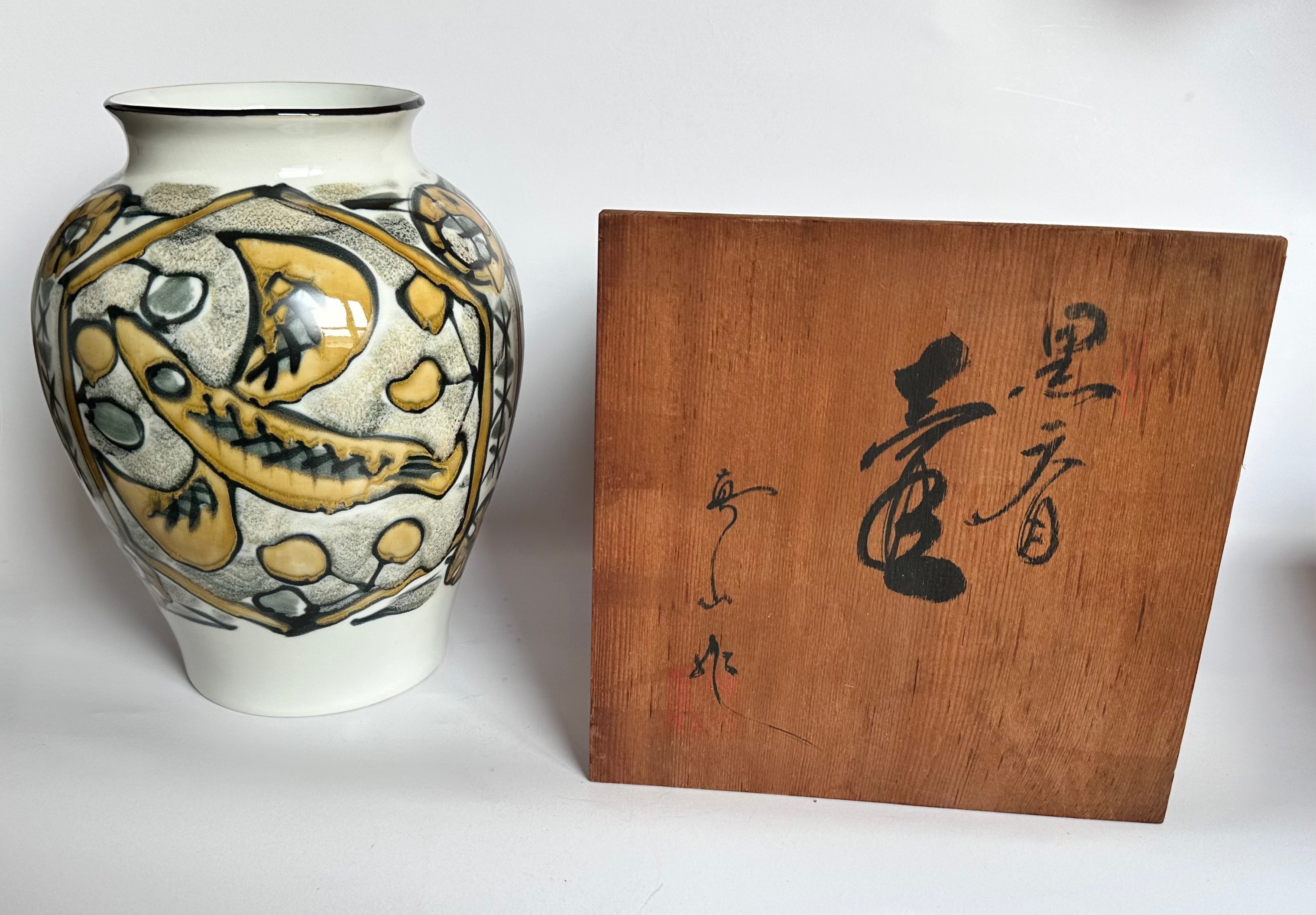 Decorative vase with fish design next to a wooden box with Japanese text on a white background
