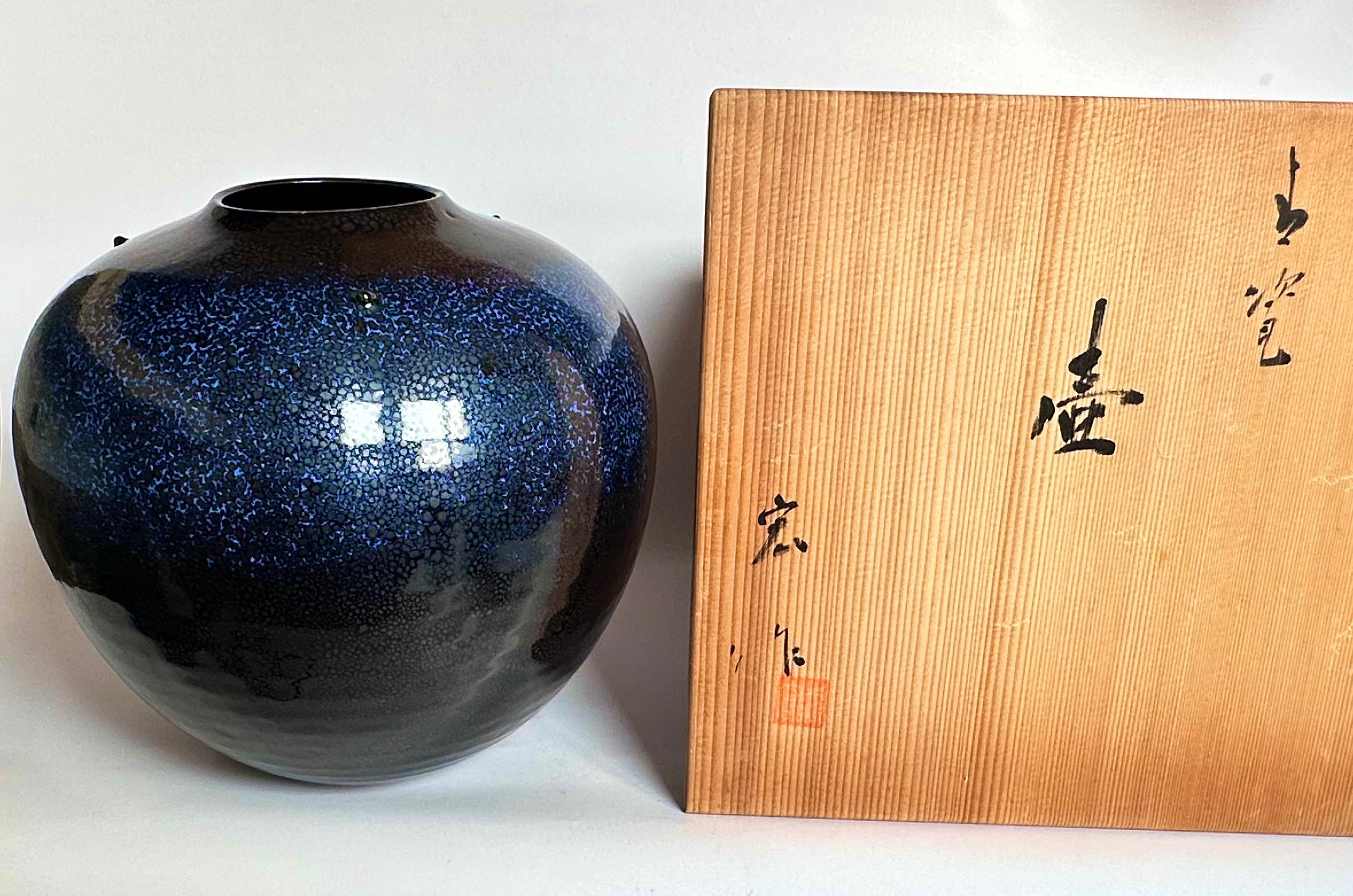 Blue ceramic vase next to a wooden box with Japanese text on a white background
