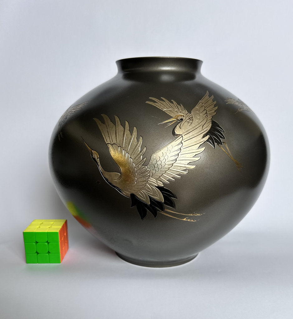 Black vase with gold bird design next to a Rubik's Cube on a light gray background