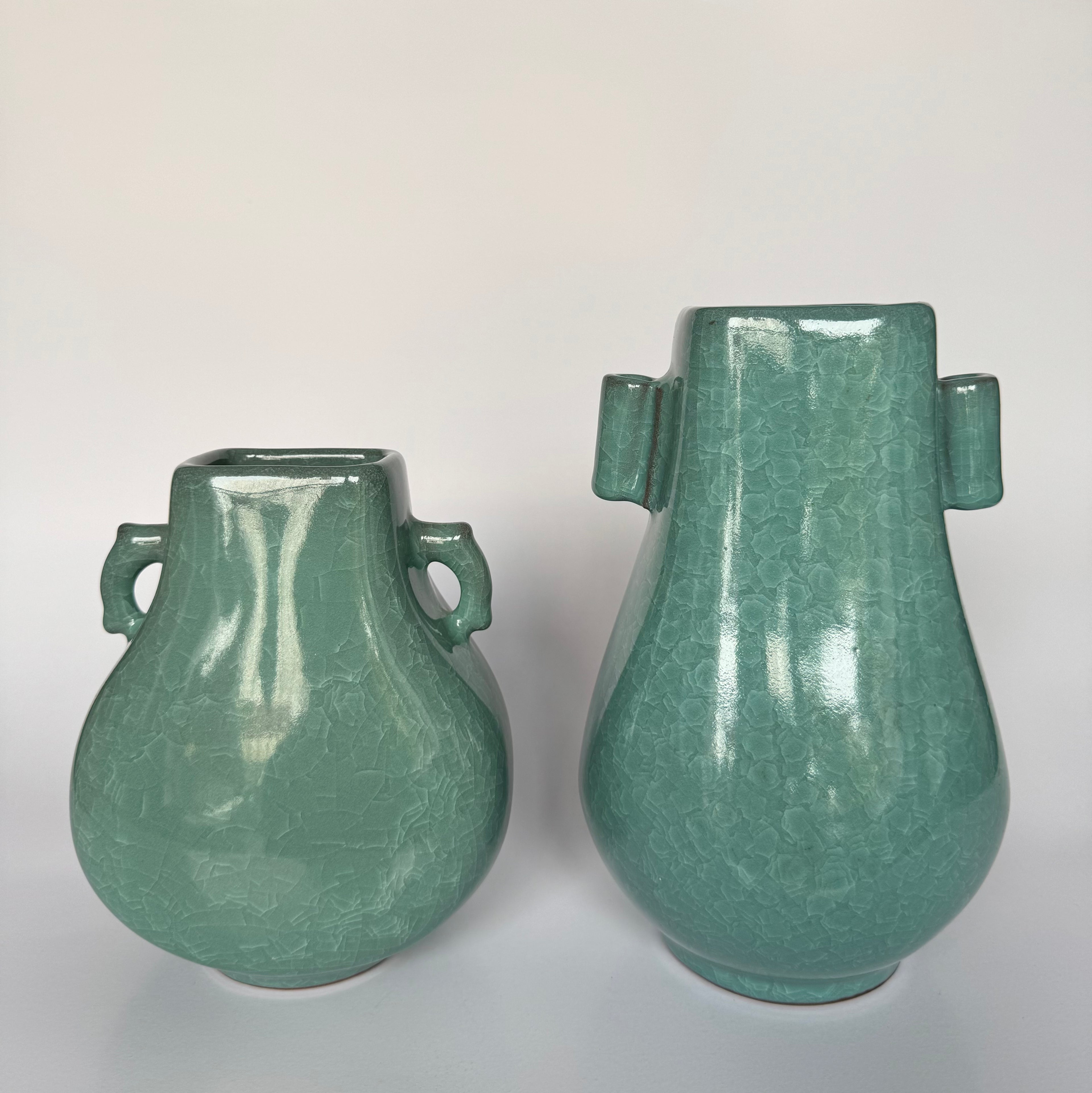 Two green ceramic vases with handles on a white background