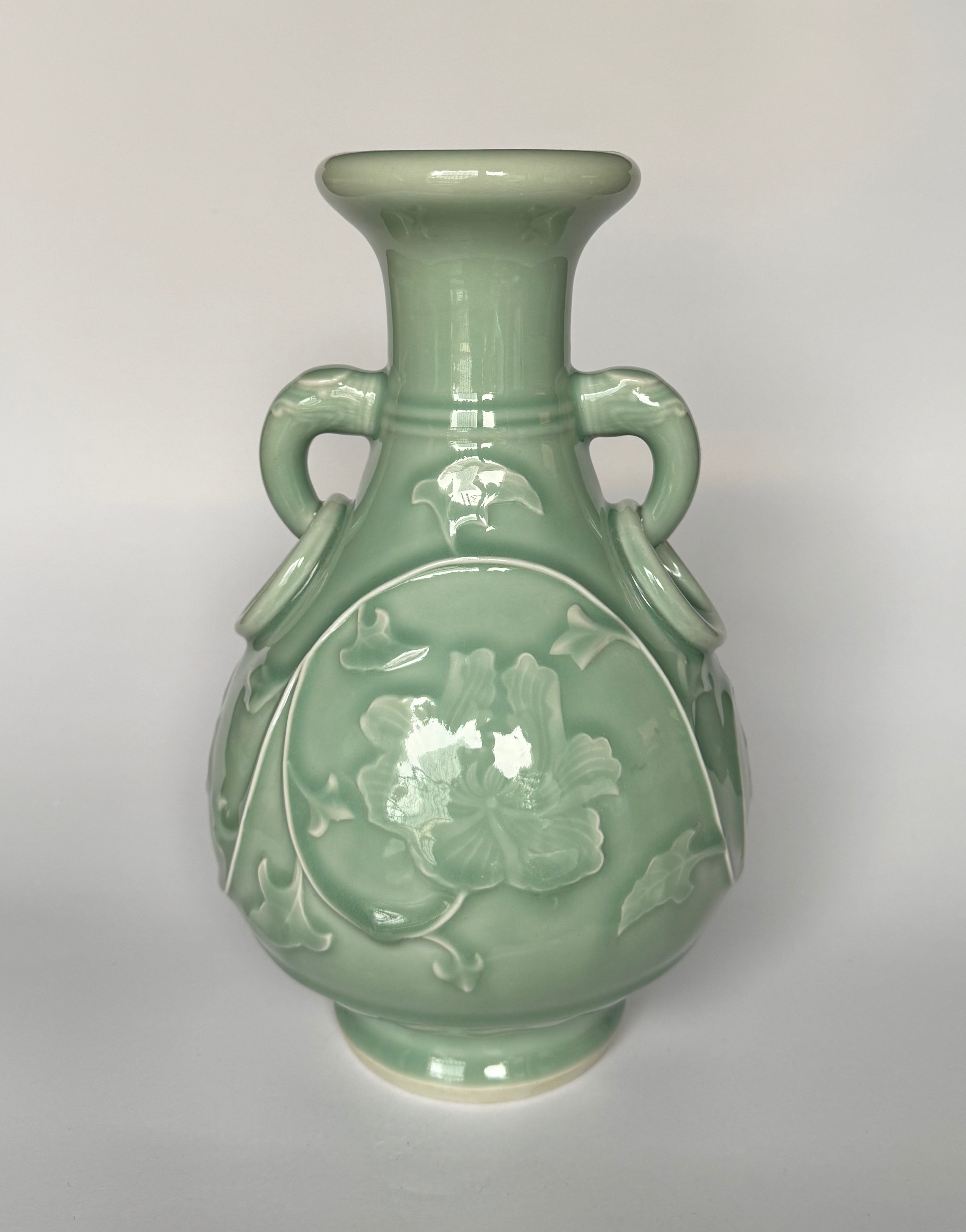 Green ceramic vase with floral design on a gray background