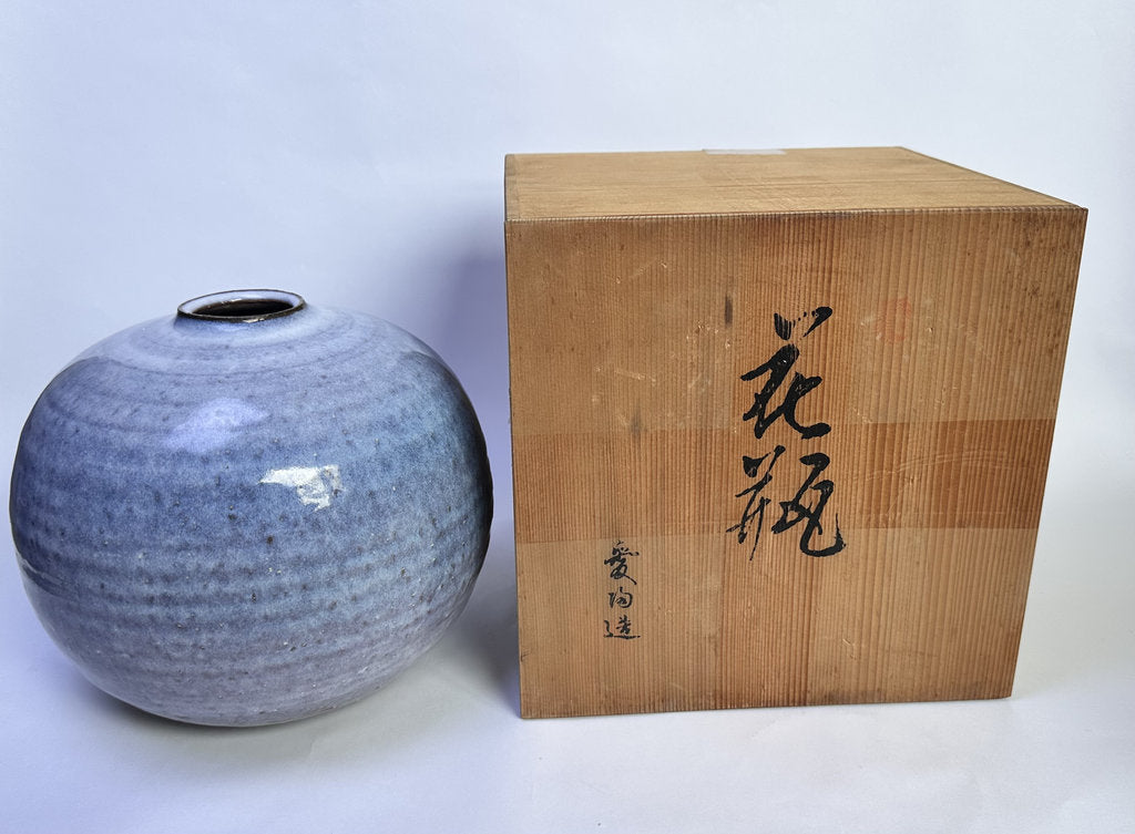A round glazed ceramic vase with a speckled gray-blue finish sits beside a light wood presentation box with black calligraphy, photographed against a plain light background.