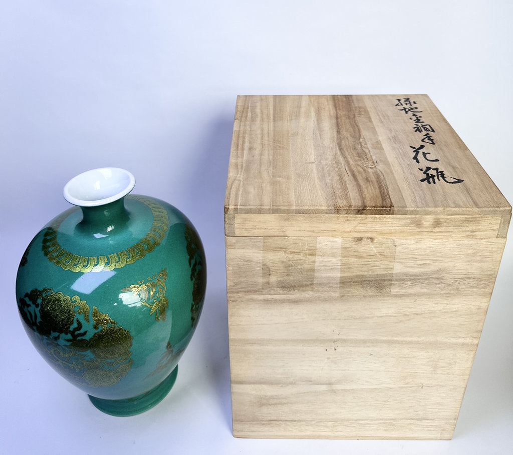 A glossy teal-green ceramic vase with gold dragon-style decoration and a white interior, shown next to a light natural wood presentation box with black Japanese characters on the lid, against a plain light background.