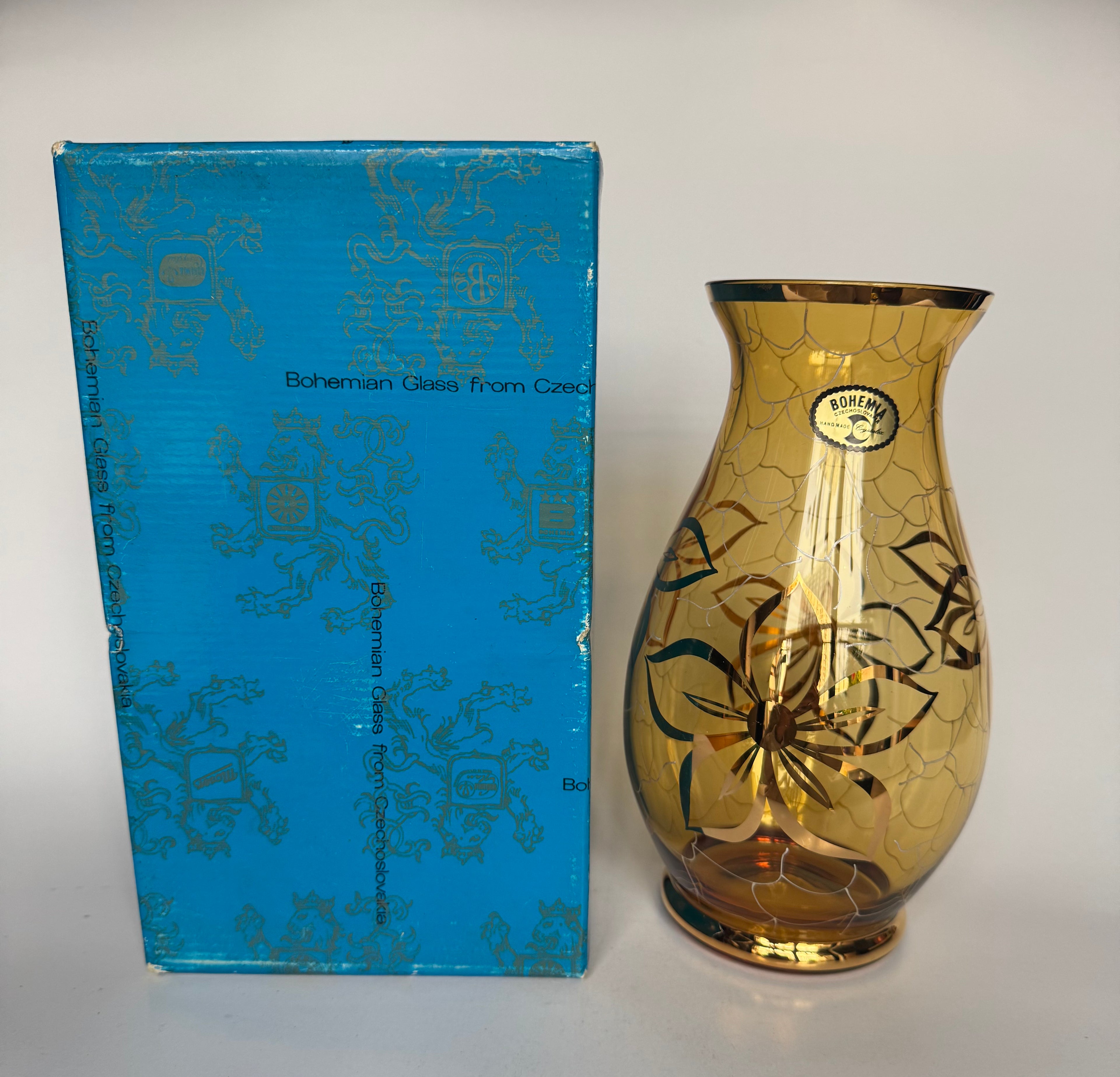 Gold glass vase with decorative patterns next to a blue box labeled 'Bohemian Glass from Czechoslovakia'.