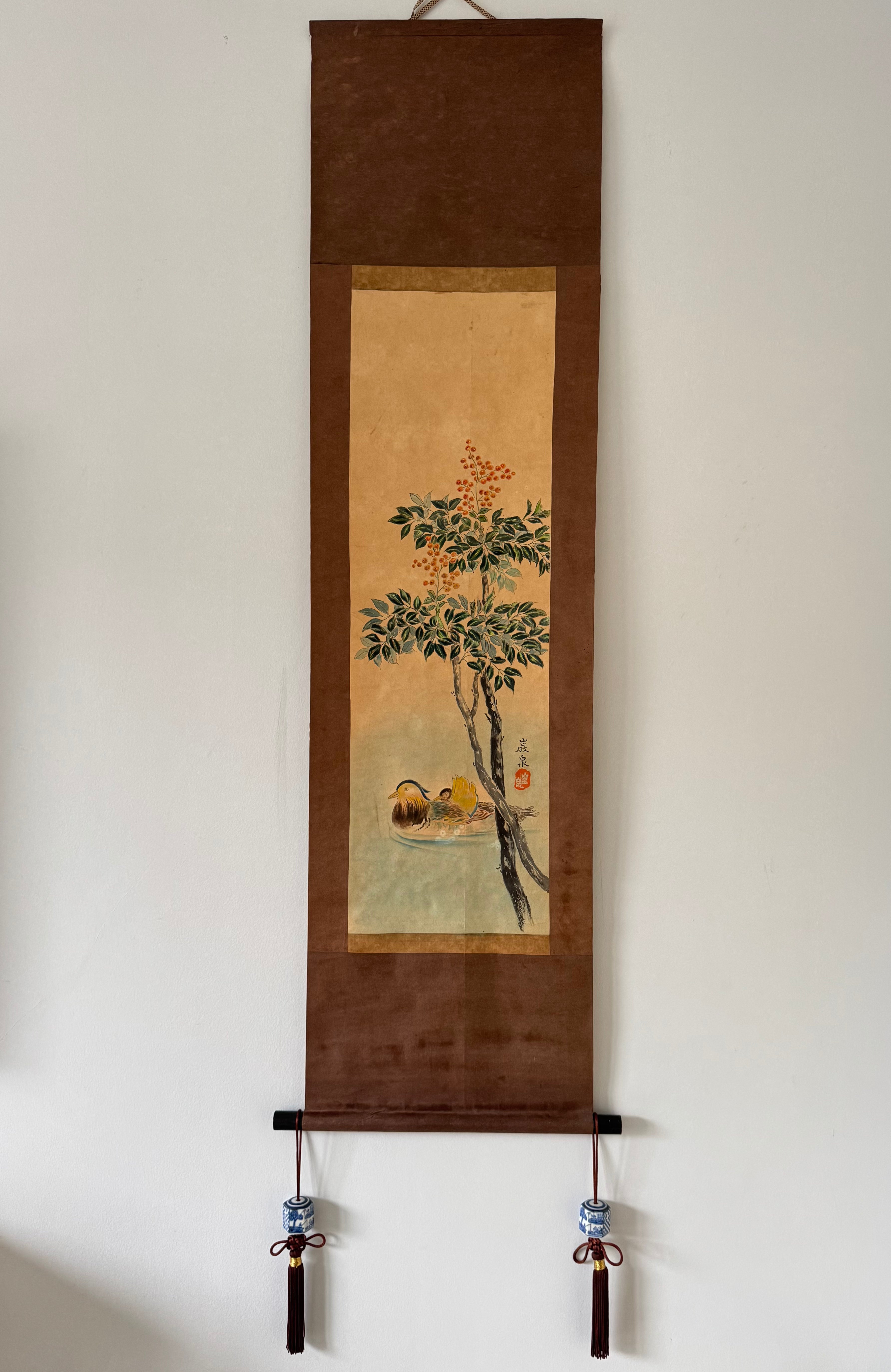 Traditional Japanese hanging scroll with a tree and landscape on a plain wall.