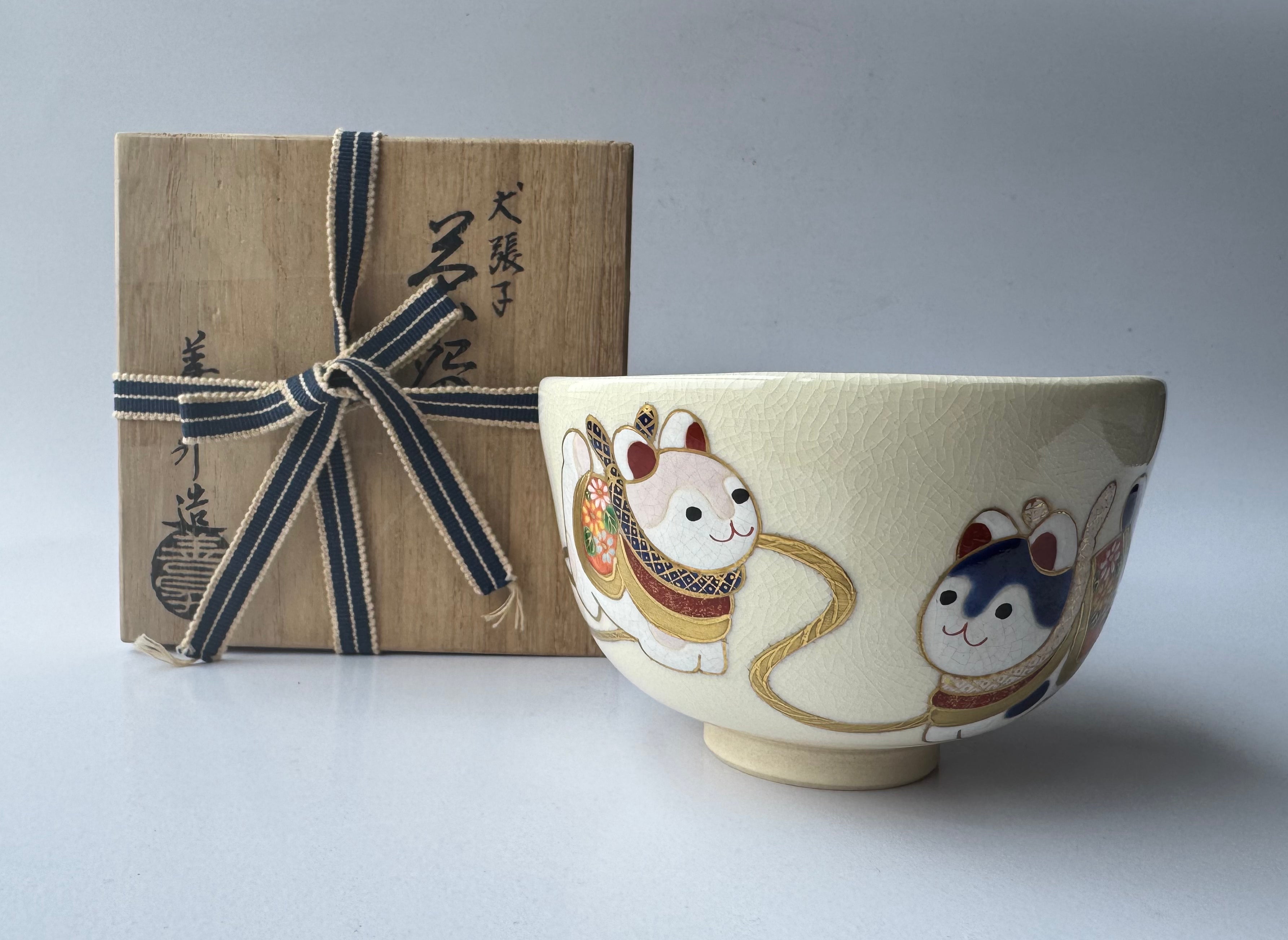 Ceramic bowl with cat illustrations next to a wrapped gift box on a light gray background