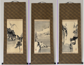 Three traditional Japanese hanging scroll paintings displayed side-by-side against a light gray wall. The scrolls feature brown patterned paper borders and depict ink wash landscapes with mountains, trees, and small buildings.