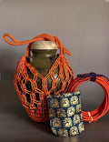 Decorative vase with orange rope netting, blue pouch with pattern, and coiled orange cable on a gray background