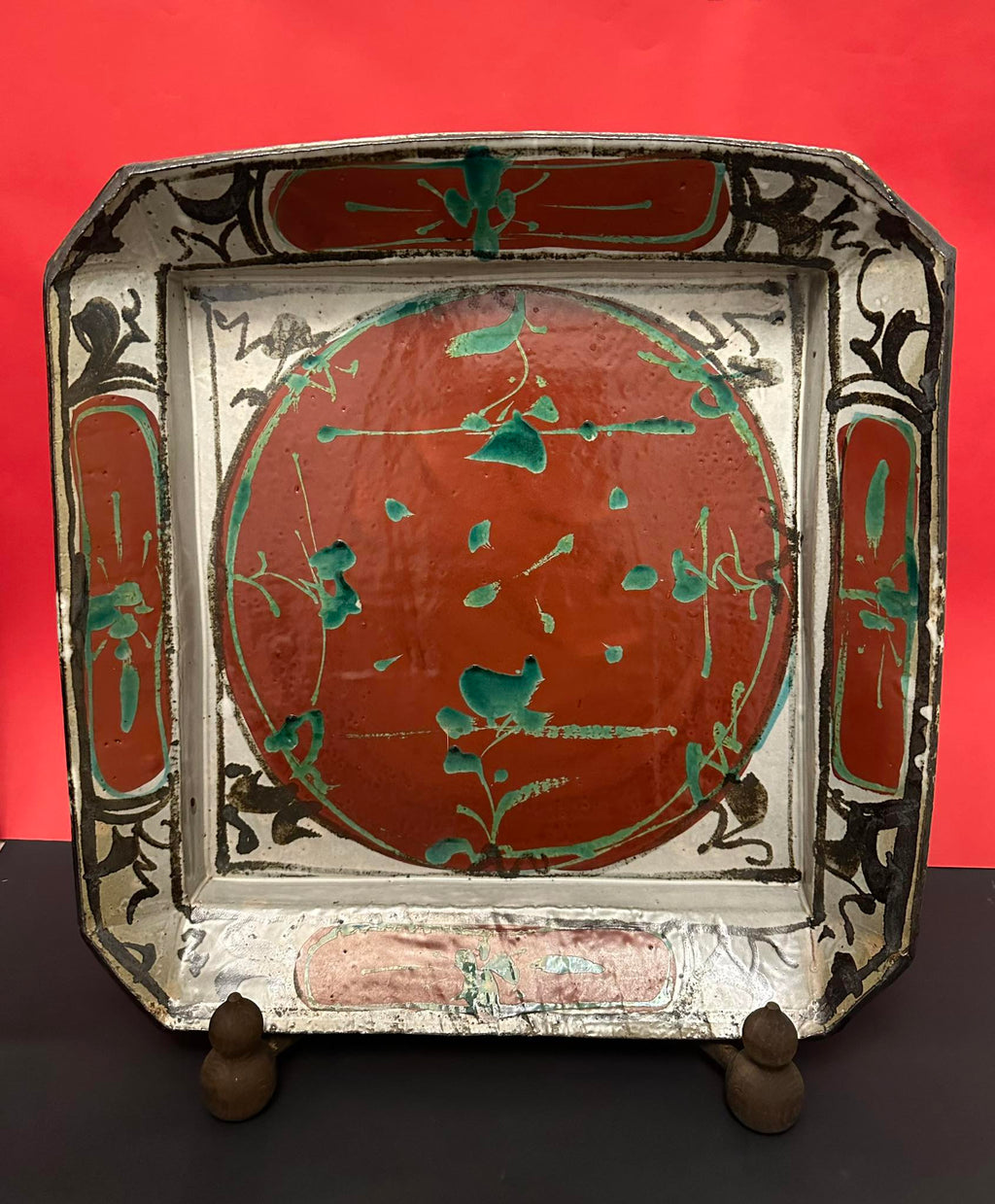 Decorative tray with red center, black and white border, and green accents on a red background