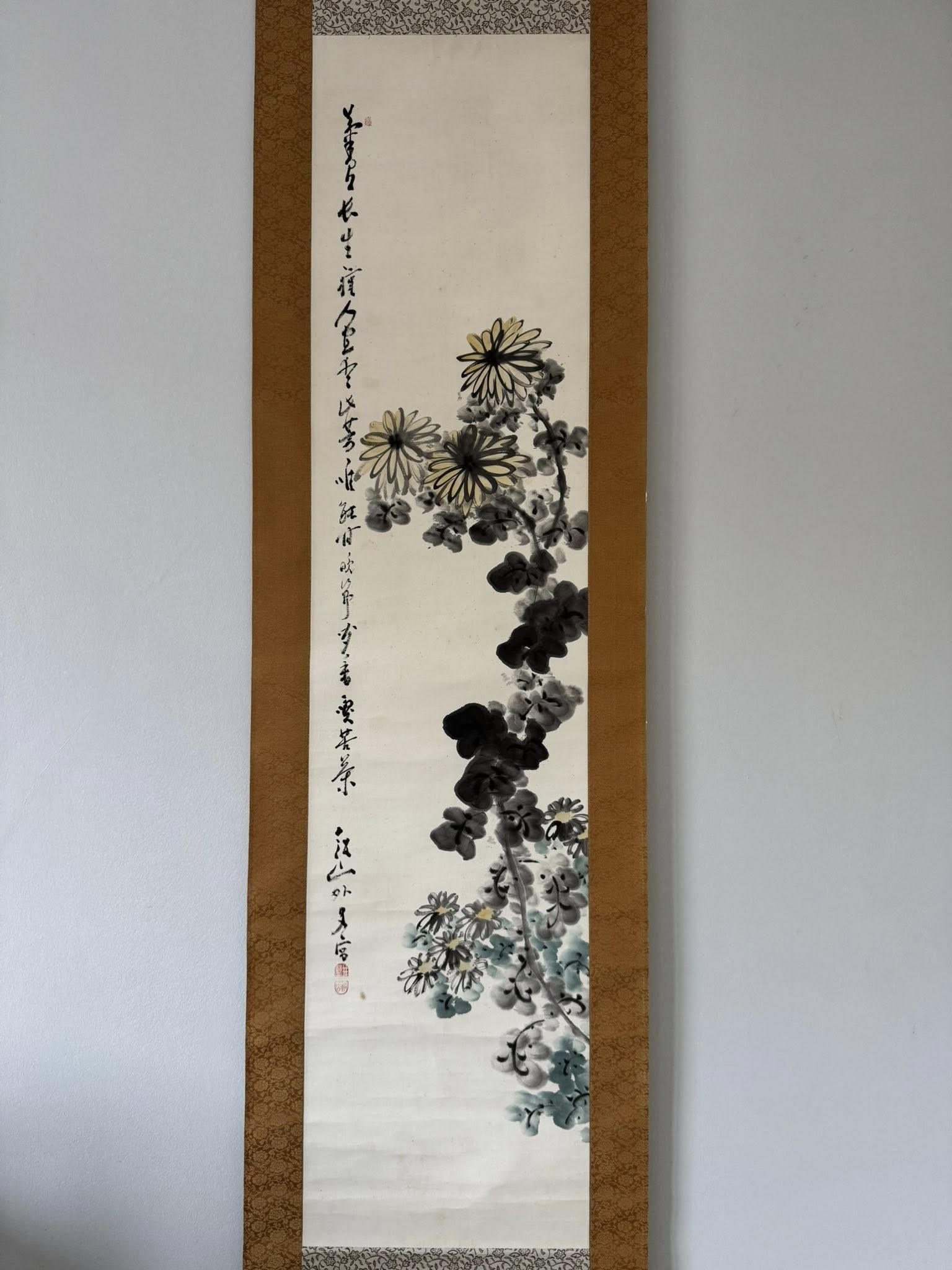 Traditional Japanese ink painting of flowers in a wooden frame on a white wall.