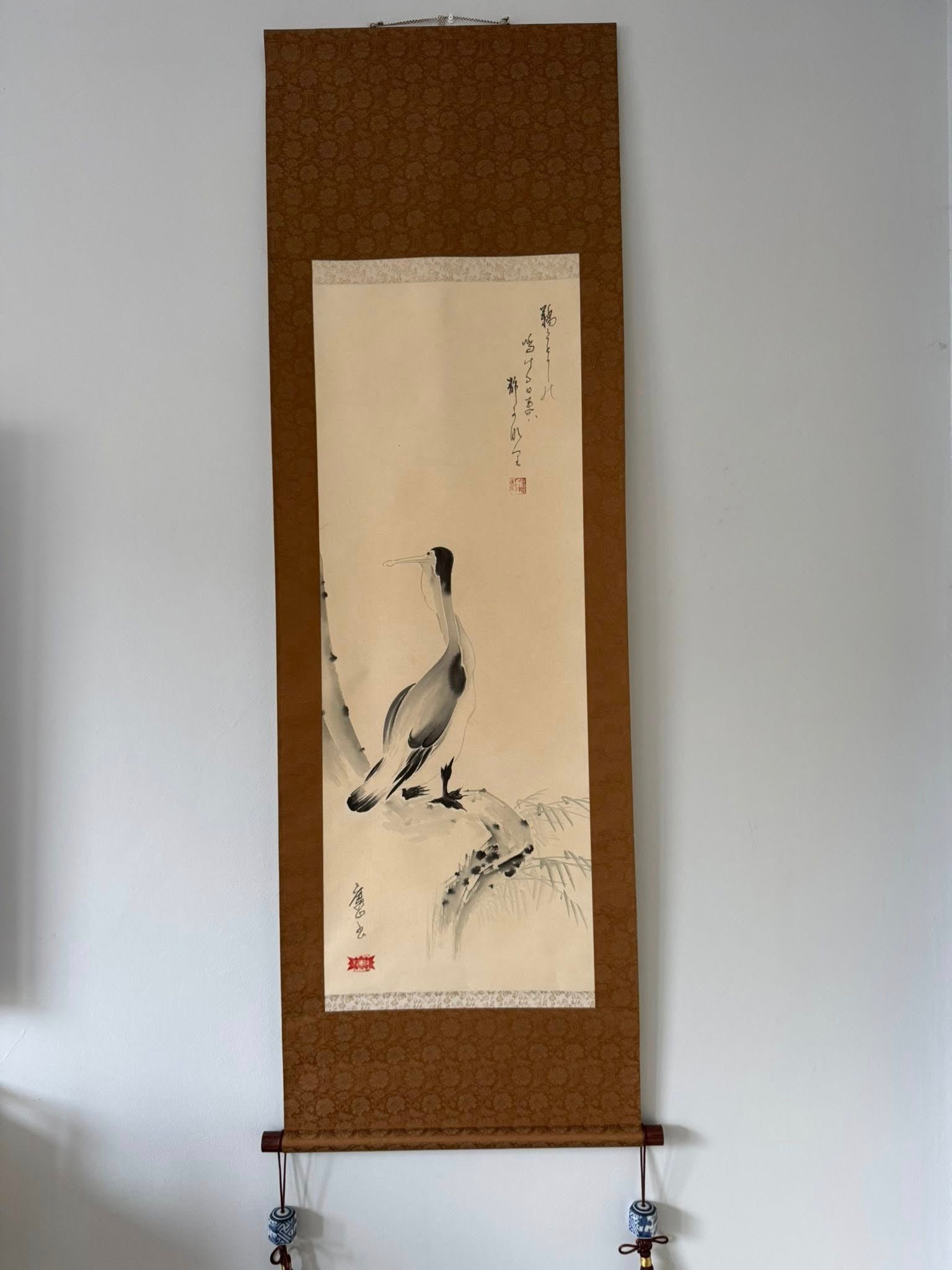 Traditional Chinese ink painting of a goose on a brown frame against a white wall.