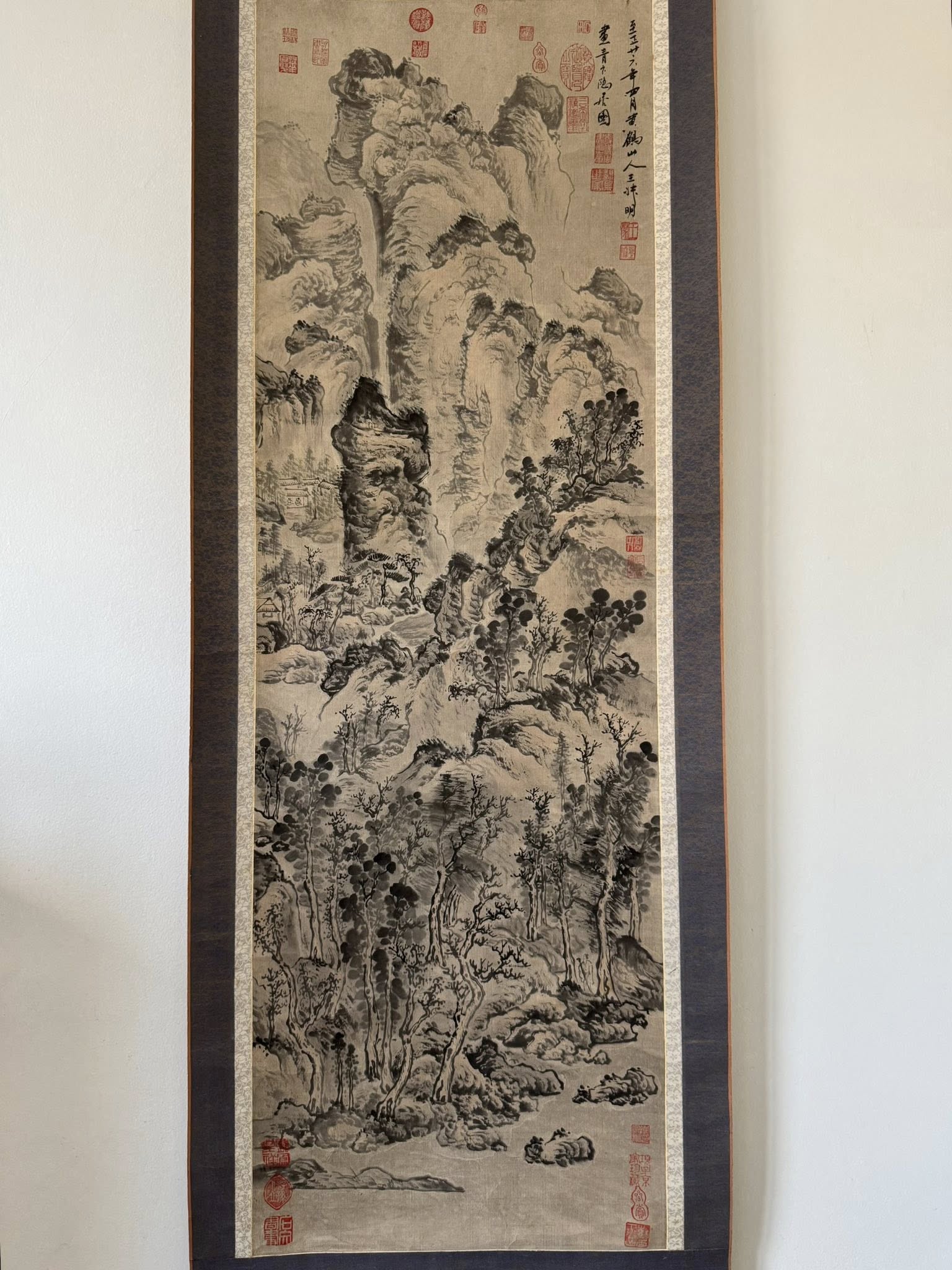 Traditional landscape painting with ink and wash on silk, framed against a white wall.
