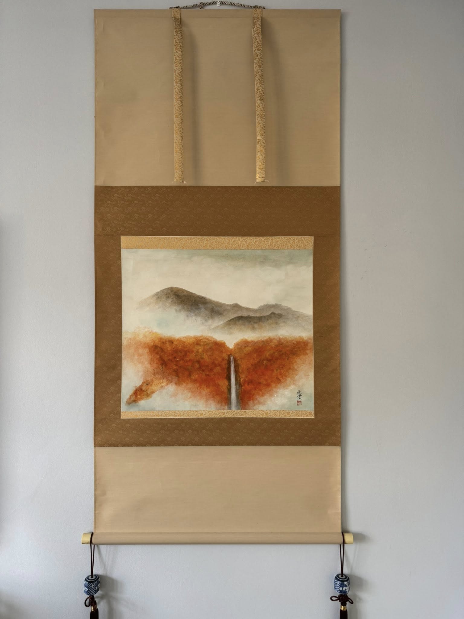Traditional Japanese landscape scroll with mountains and a red patch on a beige background